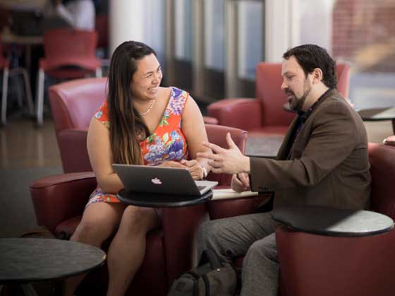 two students talking while sitting with a laptop